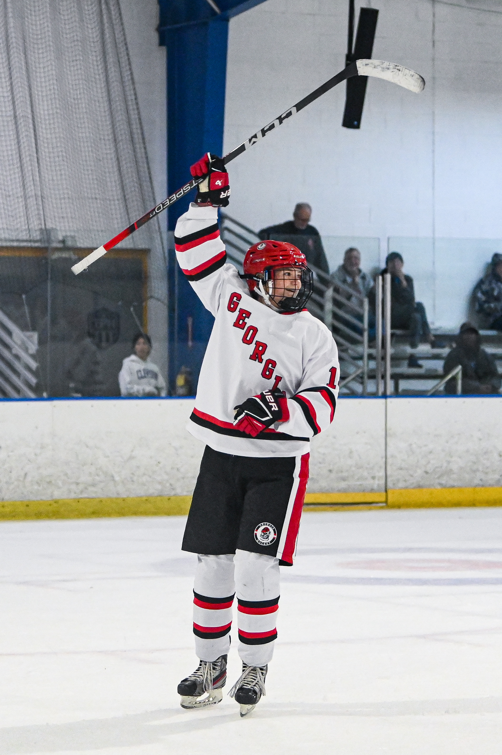 An image of Eva raising her stick in the air in celebration after assisting a goal.